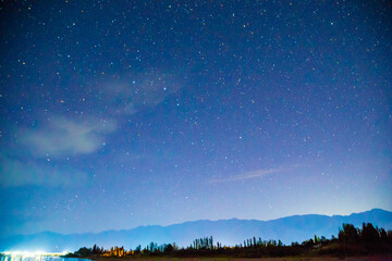 Starry sky and clouds. Night landscape, lights reflecting in the sea and mountains. Natural background