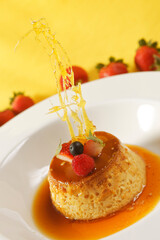 Vanilla custard with caramel and strawberry on yellow tablecloth.