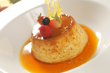 Vanilla custard with caramel and strawberry on yellow tablecloth.