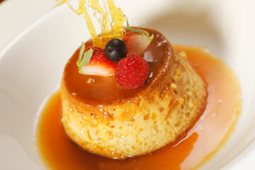 Vanilla custard with caramel and strawberry on yellow tablecloth.
