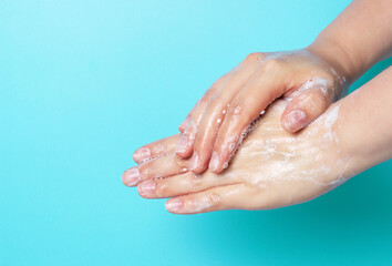Fototapeta premium The girl washes her hands with soap and foam on blue background