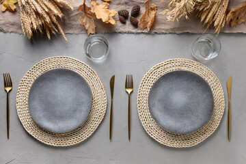 Autumn table setting with dry yellow oak leaves, fall decoration and golden cutlery on grey table. Flat lay, top view. Thanksgiving day