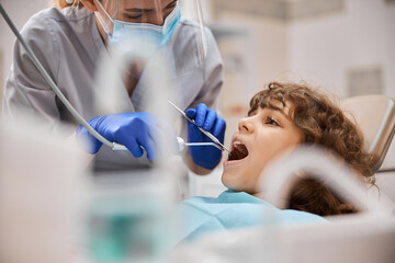 Calm child lying down in dental chair with his mouth open