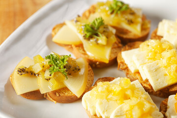 Snacks of toasted bread with Mozarella cheese, fresh cheese and Manchego cheese with strawberry, kiwi and pineapple marmalade.