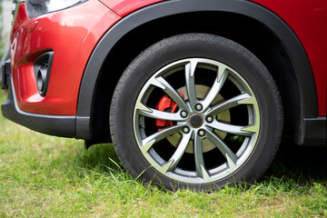 The front wheel of a red car, which is parked in the wrong place on the grass.