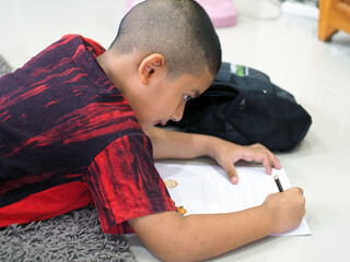 Boy is wriitng or drawing in paper.