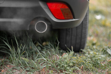 Toxic CO2 exhaust fumes from the exhaust pipe of a car parked on the lawn. Shallow depth of field,...