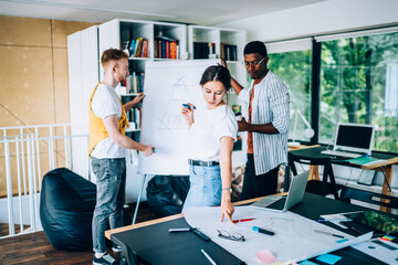 Obraz premium Young woman checking draft near diverse colleagues