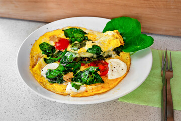 Egg omelette with spinach leaf, tomato and cheese on plate.