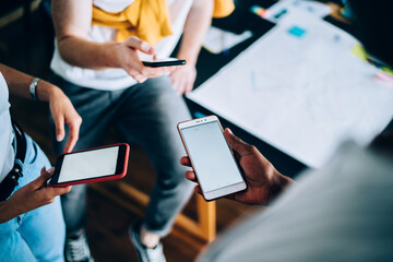 Faceless worker watching cellphone relaxing with coworkers at workplace