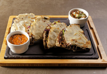 Traditional Oaxacan tlayuda stuffed with meat, melted cheese and avocado, accompanied by red chili sauce.