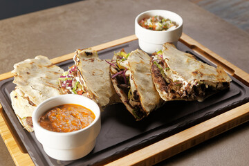 Traditional Oaxacan tlayuda stuffed with meat, melted cheese and avocado, accompanied by red chili sauce.