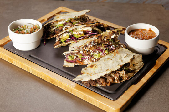 Traditional Oaxacan tlayuda stuffed with meat, melted cheese and avocado, accompanied by red chili sauce.