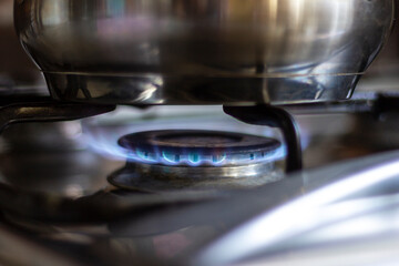 Close-up of a stainless steel pot standing on a kitchen stove with a gas burner on.