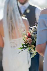 close up of bridesmaid bouquet with bride and groom blurry in background during ceremony