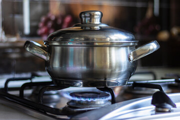 Close-up of a stainless steel pot standing on a kitchen stove with a gas burner on.