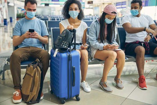 Young calm group of people in the airport with baggage sitting on the bench