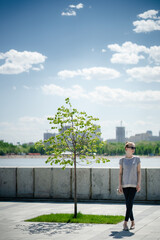 A young caucasian woman in sunglasses in a city park near the river on a sunny summer day. Reflections alone, vacation in an urban environment or summer walks concept.