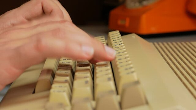 Typing on old computer and an orange rotary phone in the background (close up)