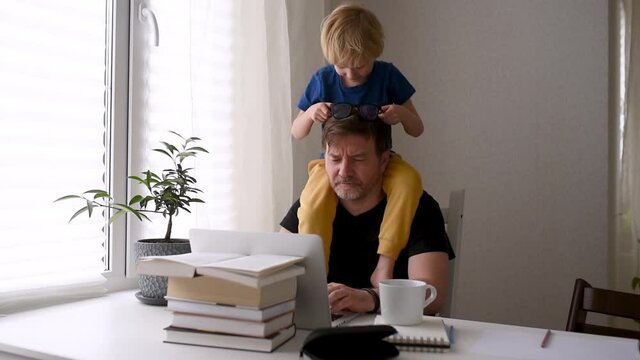 Man working from home with laptop during quarantine. Home office and parenthood at same time. Exhausted parent with hyperactive child. Chaos with kids during isolation