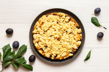 Delicious juicy plum cake in a round plate on a white wooden background, plum tree leaves with fruits