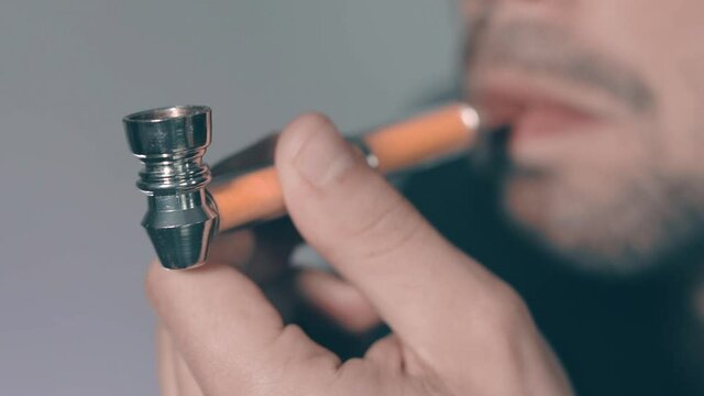 Young Man in Black Shirt Smoking Weed Indoors Using Pipe. Relaxation due to Ganja. Marijuana Culture Concept - Slow Motion. Big Close-Up View, Dynamic Shot
