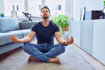 Handsome man meditating at home sitting on the floor