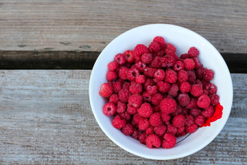 Top view of a white plate with fresh forest raspberries, standing on the right on a gray wooden bench. Eco-friendly, healthy food.