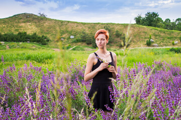 portrait of a red-haired, short-haired, young woman in a black dress, against a background of blue wildflowers (Aconite Dzungarian) mountains and sky, the concept of natural beauty
