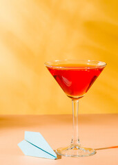 Vacation red cocktail in martini glass with blue paper plane  on yellow background