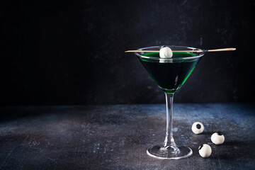 Halloween coctail black widow with green drinks with eyes in glass on dark background