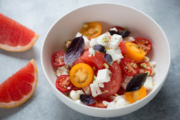 Salad with grapefruit, feta cheese, red and yellow cherry tomatoes, nuts and red basil served in a white bowl, studio shot