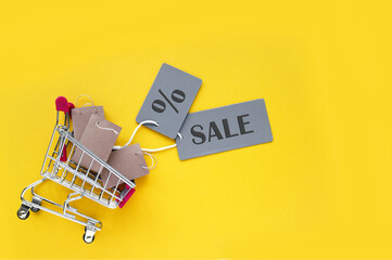 Mini shopping cart with small craft bags and gray labels with an inscription SALE on a yellow...