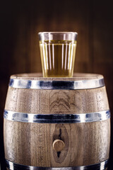 aged oak barrel with glass of distilled beverage used for fermented drinks such as rum, cachaça, vodka, among others. Spot focus on the barrel.
