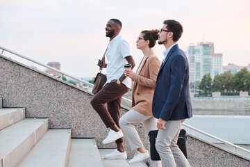 Side view of confident multi-ethnic students chatting and moving up stairs while walking into university