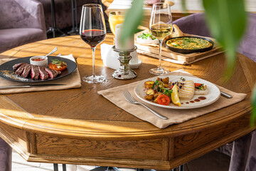 table covered with food and drinks. Steak, grilled squid with vegetables, scrambled eggs with dill, parsley and vegetables.