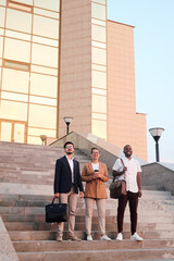 Portrait of ambitious young multi-ethnic students standing on step against university