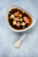 Bowl of miso soup with salmon and tofu over light-blue stone background, studio shot, view from above