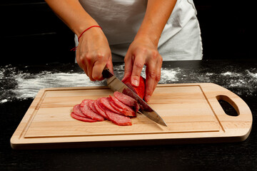 girl chef cuts salami sausage for making homemade italian pizza on a wooden cutting board