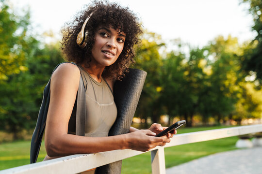 Image of african american sportswoman using cellphone and headphones