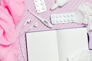 Obraz na płótnie Canvas Open notebook. Nearby are a white thermometer, white pills, medicines, nasal spray, crumpled paper napkins. In addition, there is a pink scarf and headphones. Notebook on a pink knitted background