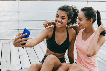 Image of happy multinational sportswomen taking selfie on cellphone while sitting