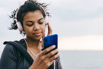 Image of pleased african american woman using cellphone and headphones