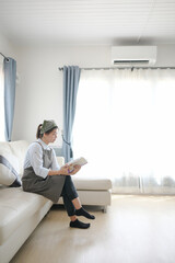 The housewife sat in the living room inside the house. There is air conditioning on the wall above the ceiling of the room.