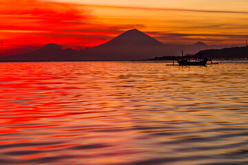Silhouette of a volcano over water in a vivid sunset in Indonesia