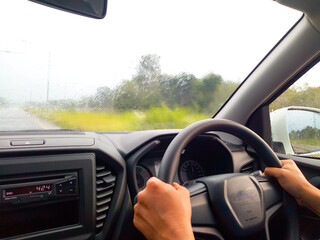 An Asian man's hand steering a car When it rains on the streets of Thailand