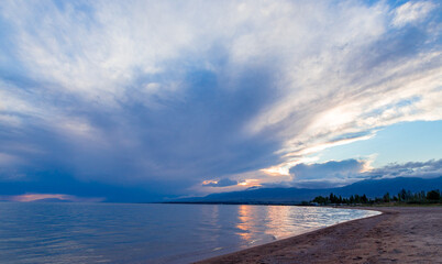 Obraz premium Beautiful sunset by the lake. Bright clouds are reflected in the water. Kyrgyzstan.