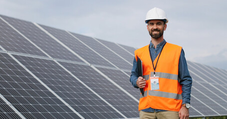 Portrait of electrician in safety helmet and uniform on background field of photovoltaic solar...