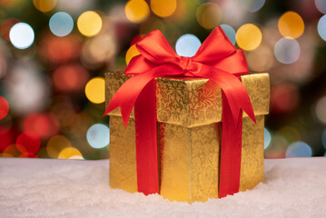 Christmas gold gift box against beautiful bokeh background. gift in gold paper with red bow