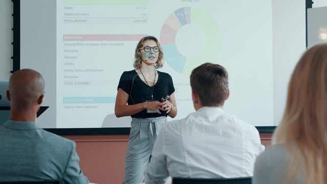 Businesswoman standing in front of a projection screen and presenting her ideas to group of people sitting in a seminar. Female professionals addressing a business conference.
